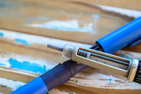 Close-up of a blue medical insulin pen injector resting on a rustic wooden surface, highlighting the needle tip and medication reservoir for diabetes management and hormone therapy treatment