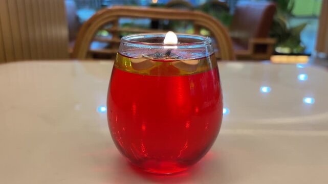 Video Decorative table candles placed in a round glass container. These candles use red liquid fuel, usually paraffin oil or perfume oil, with a floating wick on top.
