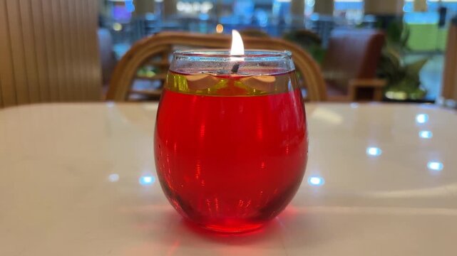 Video Decorative table candles placed in a round glass container. These candles use red liquid fuel, usually paraffin oil or perfume oil, with a floating wick on top.