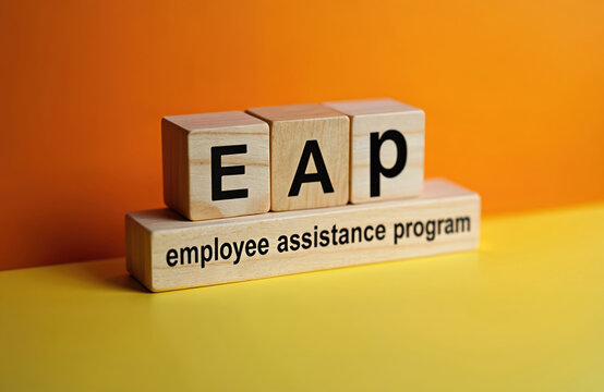 Wooden blocks spell out EAP initials, with the full phrase employee assistance program below. Concept represents corporate support for worker mental health, personal issues, and workplace well-being.