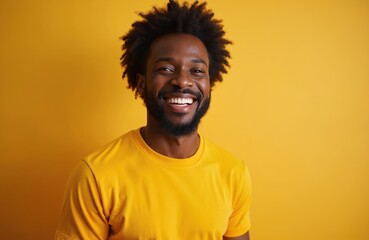 Fototapeta premium Black man with afro hair smiles brightly. He wears a yellow t-shirt against a solid yellow backdrop. Casual portrait conveys joy and confidence. Modern studio shot.