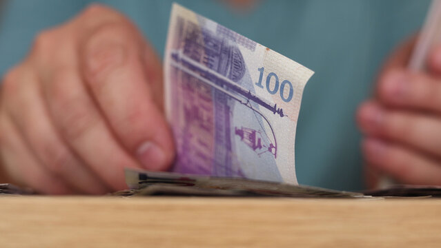 Horizontal mobile photo close up. Man counts lilac purple paper banknote One hundred lari on wood table. 100 GEL bill. Georgian cash money. Concept of loan, wages, debt, credit, pay tax, bribe, budget