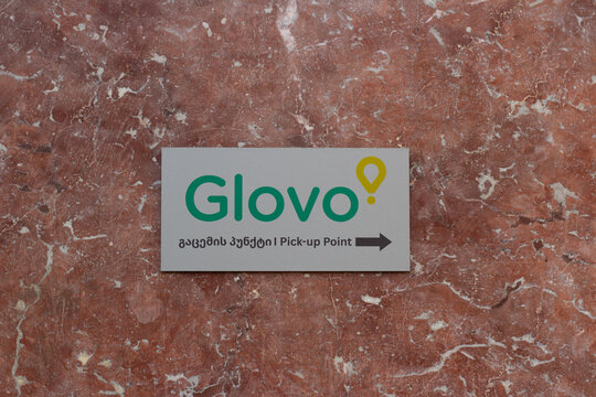Tbilisi, Georgia - January 20, 2026: Horizontal street city photo. Sign board with Glovo logo on red marble wall. Translation from Georgian: Pick-up point. Concept of food, drink, lunch, dinner, job