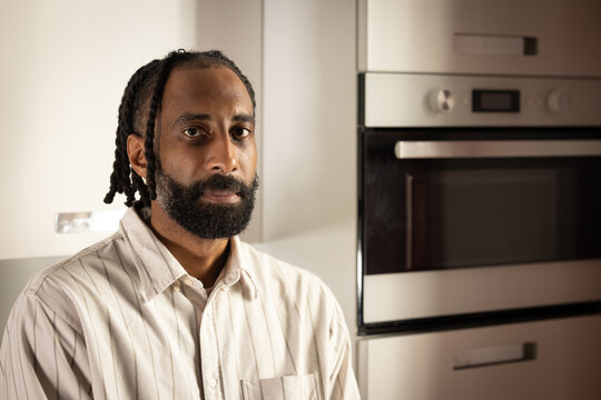 portrait d'un beau jeune homme noir portant une barbe, souriant, qui est debout chez lui dans sa cuisine