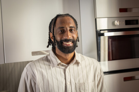 portrait d'un beau jeune homme noir portant une barbe, souriant, qui est debout chez lui dans sa cuisine