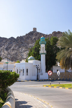 Muscat, Oman &ndash; December 28, 2025: Traditional mosque with a turquoise dome and slender minaret located in a quiet residential area of Muscat, set against rugged rocky mountains under a clear blue sky.
