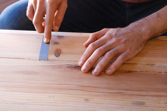 Male hands carefully apply wood filler with a spatula during the restoration of a chest.