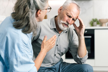 Elderly man suffers severe headache while wife support him at home