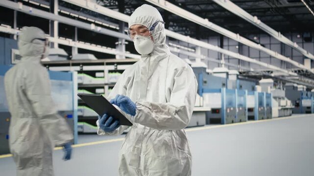 Engineer walking in semiconductor production plant floor, using tablet to do maintenance on automated machinery. Man in safety equipment checking PCB factory hardware with device, camera A