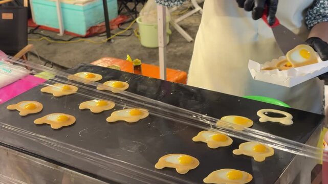A cinematic 4K horizontal video showcasing a street food vendor preparing mini pancakes or "Tokyo-style" crepes with egg on a flat griddle.