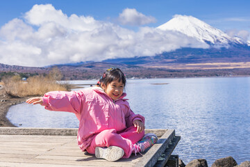 Fototapeta premium Child happily sitting on a wooden pier overlooking lake yamanakako and mount fuji