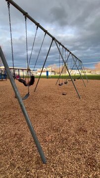 Child on swing at an empty playground during the day under overcast sky. In vertical format.