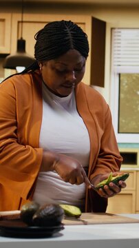 Cutting avocado, cooking video, recipe preparation on toast, black woman, food vlogger working at the counter. Influencer explaining culinary tutorial and meal prep, nutritious healthy choice.