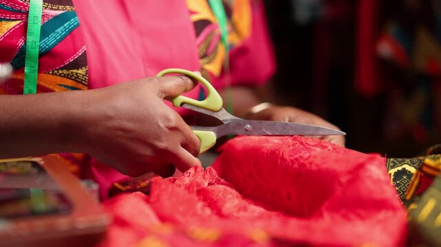 African tailor's hands cutting colorful wax print fabric with scissors in a sewing workshop