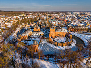 Naklejka premium Aerial view of the medieval Huis Bergh Castle in s-Heerenberg, Netherlands. A stunning winter scene with a snow covered fortress, frozen moat, and a charming European town during golden hour.