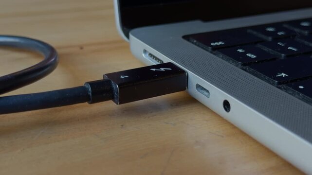 Laptop port with connected cable. Scene depicting USB cable plugged into laptop for charging and data transfer