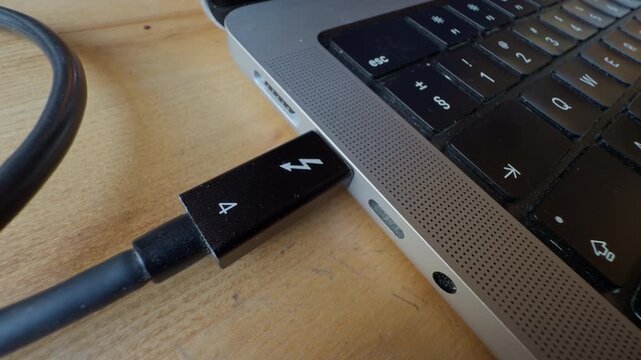 Laptop cable setup. Remote work scene with thunderbolt cable plugged into laptop on warm lit wooden surface