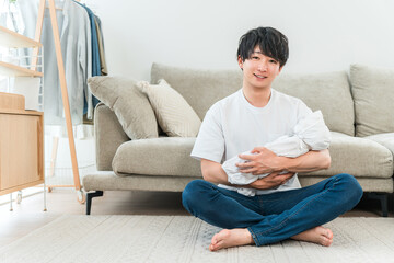Fototapeta premium A young Asian man holding a baby in his living room.