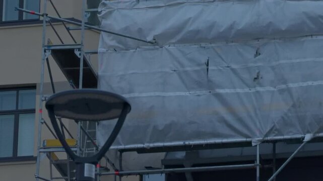 Facade covering shown. Construction workers operate behind mesh coverings and tarpaulins shielding building retrofit
