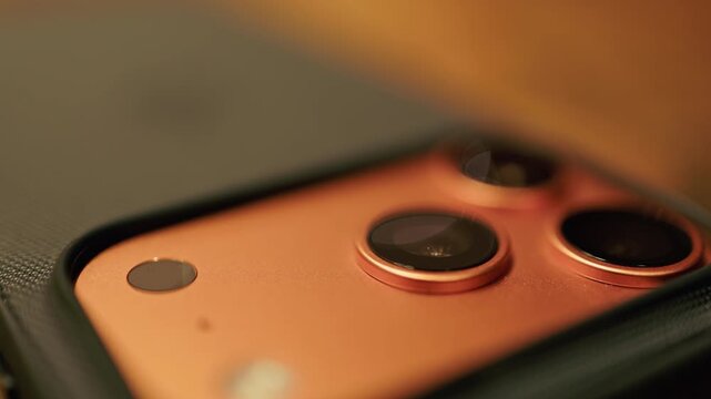 Closeup of smartphone camera with warm lighting. Triple lens module with reflective glass and detailed metal work