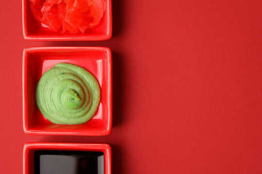 Bowls with wasabi, soy sauce and pickled ginger on red background, closeup