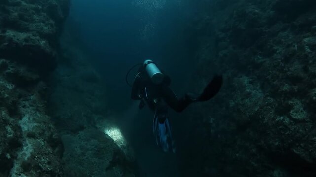 A solitary diver explores a dark underwater cavern with a flashlight
