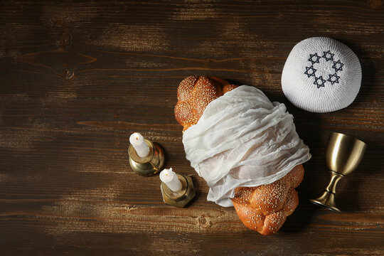 Traditional challah bread with wine goblet, kipa and burning candles on wooden table. Shabbat Shalom