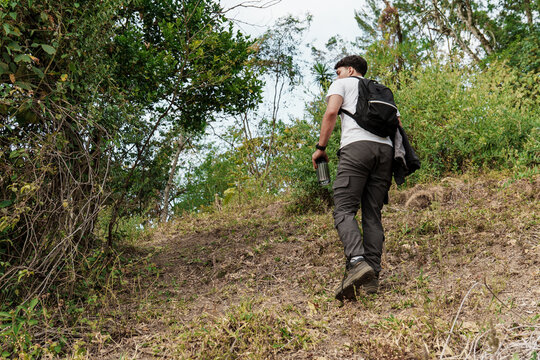 Young man hiking uphill through green forest outdoors