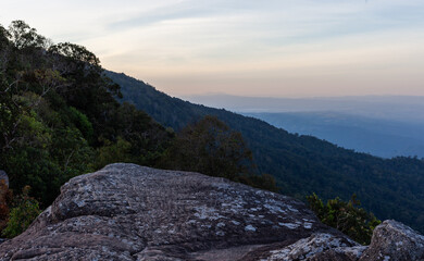 Obraz premium Phu Hin Rong Kla National Park mountain landscape at sunrise. Rugged rocky terrain with forested hills. Hazy sky above a scenic natural view in Thailand.