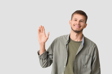 Fototapeta premium Handsome young stylish happy man waving hand on grey background