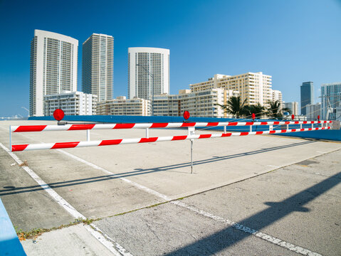 Closed road on a bascule bridge with red and white striped barrier gate and traffic lights against modern skyscrapers in Florida.
