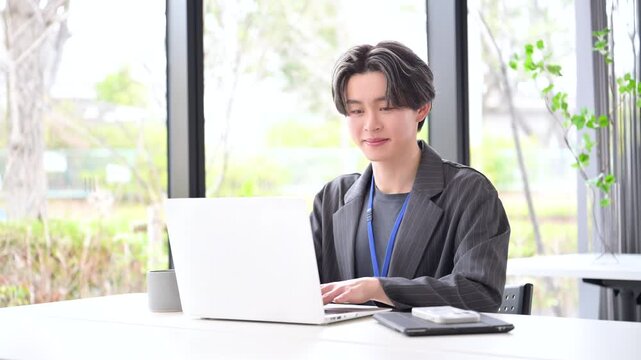 爽やかな窓辺の会社でパソコンでタイピングで仕事する若いビジネスマン　頷く理解するポーズ　若手社員の爽やかな成長と成功のビジネスシーンの動画
