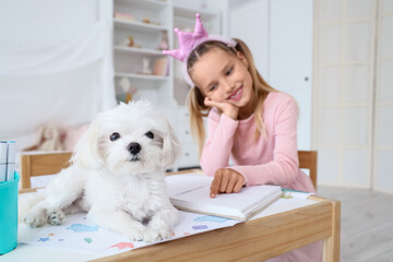 Fototapeta premium Cute little happy girl with Maltese dog reading book at table in children's bedroom