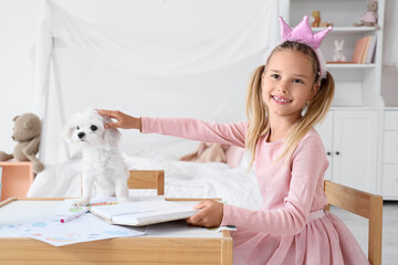 Fototapeta premium Cute little happy girl with Maltese dog reading book at table in children's bedroom