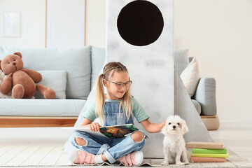 Fototapeta premium Cute little happy girl with Maltese dog and books sitting on floor near cardboard space rocket at home