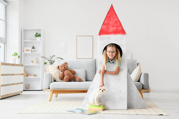 Fototapeta premium Cute little happy girl with Maltese dog and books in cardboard space rocket at home