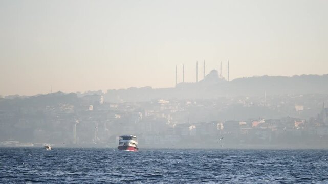 A cinematic video capturing a ferry crossing the Bosphorus Strait with Istanbul city skyline and the majestic Camlica Mosque in the background under a clear sky