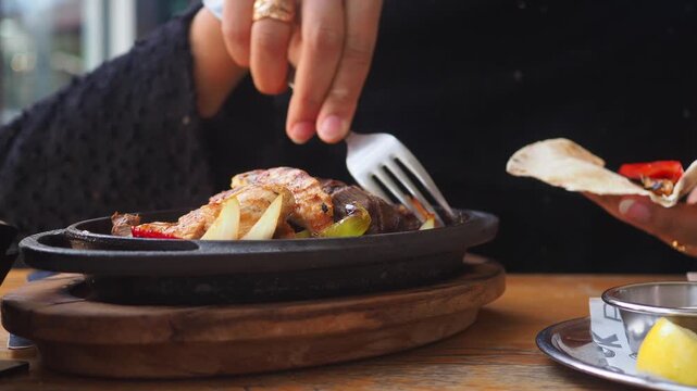Woman hands cooking chicken and pepper fajitas on a hot pan, placing the food in a flat bread to create a delicious homemade taco with fresh ingredients