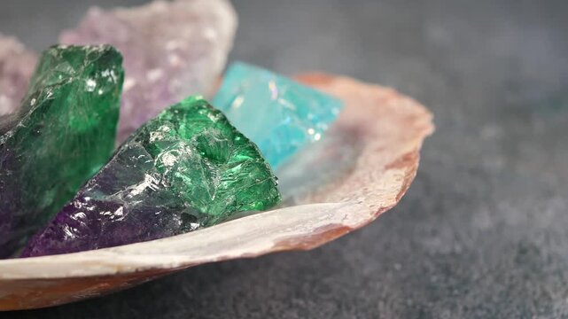 Slow panning over colorful collection of raw amethyst and emerald crystals in large seashell