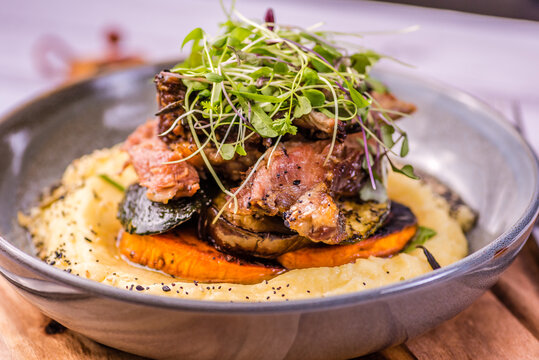 Slow-cooked lamb shank served on creamy mashed potatoes, garnished with fresh herbs in a rustic restaurant setting.