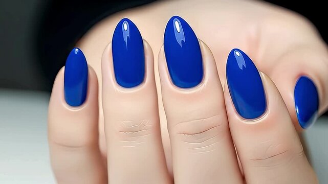 A captivating close-up showcases a female hand with impeccably manicured nails, adorned in a striking, glossy electric blue polish. The elegant almond or stiletto shape of the nails is perfectly highl