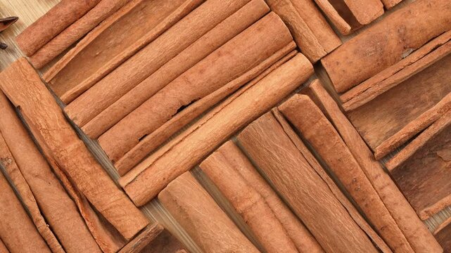 Detailed macro flat lay of rotating cinnamon sticks on a wooden board. Clean organic spice texture for baking, culinary and traditional medicine.