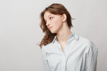 Obraz premium Young woman with curly brown hair wearing a white shirt looks sideways against a plain light background. Concept of natural beauty, casual style, and thoughtful mood in studio.