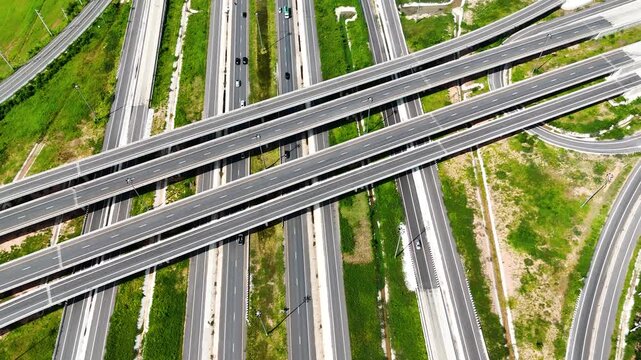 Aerial view of modern highway interchange with multilayer roads and curved ramps surrounded by green farmland, showcasing transportation infrastructure, urban development, and road network planning.