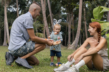 Fototapeta premium A father playfully tosses decorated Easter eggs as a toddler reacts with joy, capturing a fun outdoor family celebration on the grass.