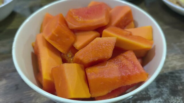 Freshly sliced ripe papaya chunks sit in a clean bowl. This vibrant orange fruit is perfectly prepared for a healthy snack. It is served chilled and ready for immediate consumption.