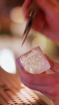 Vertical video. Pub ice. Preparing cold drink. Bartender hand using chipper making textured huge cube for refreshing cocktail. Professional bar picks chisel.