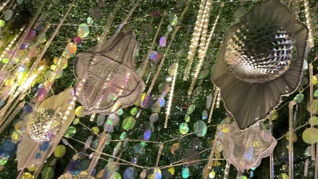 4k video of Hanging silver reflective and shimmering decoration with baubles and tassels, with green vertical garden ceiling, hanging plants from above. Festive organic natural decoration. 