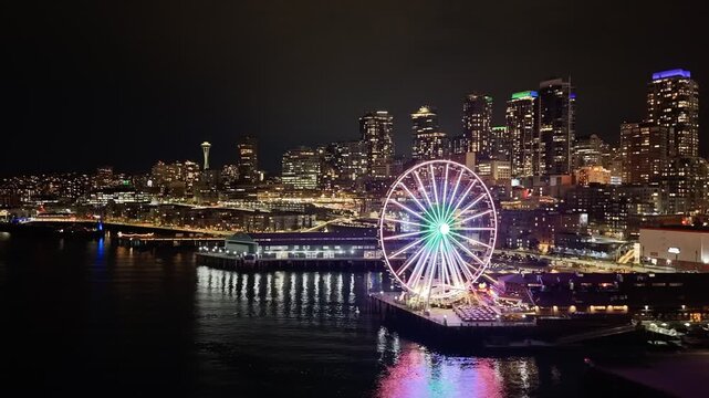 Seattle downtown skyline and waterfront with illuminated ferris wheel reflecting on Elliott Bay at night aerial view. g.