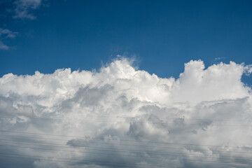 Fototapeta premium Large white cumulus clouds in blue sky behind power lines
